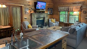 A cabin interior with a stone fireplace, wooden walls, a television, a dining area, and a sofa. - Cutest, comfiest log cabin with great screened in porch! (Sevierville)