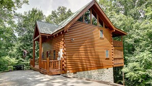 A log cabin with a porch, a small balcony, and a stone foundation.