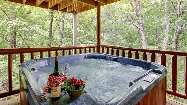 A hot tub with a wooden deck and a view of a forest.