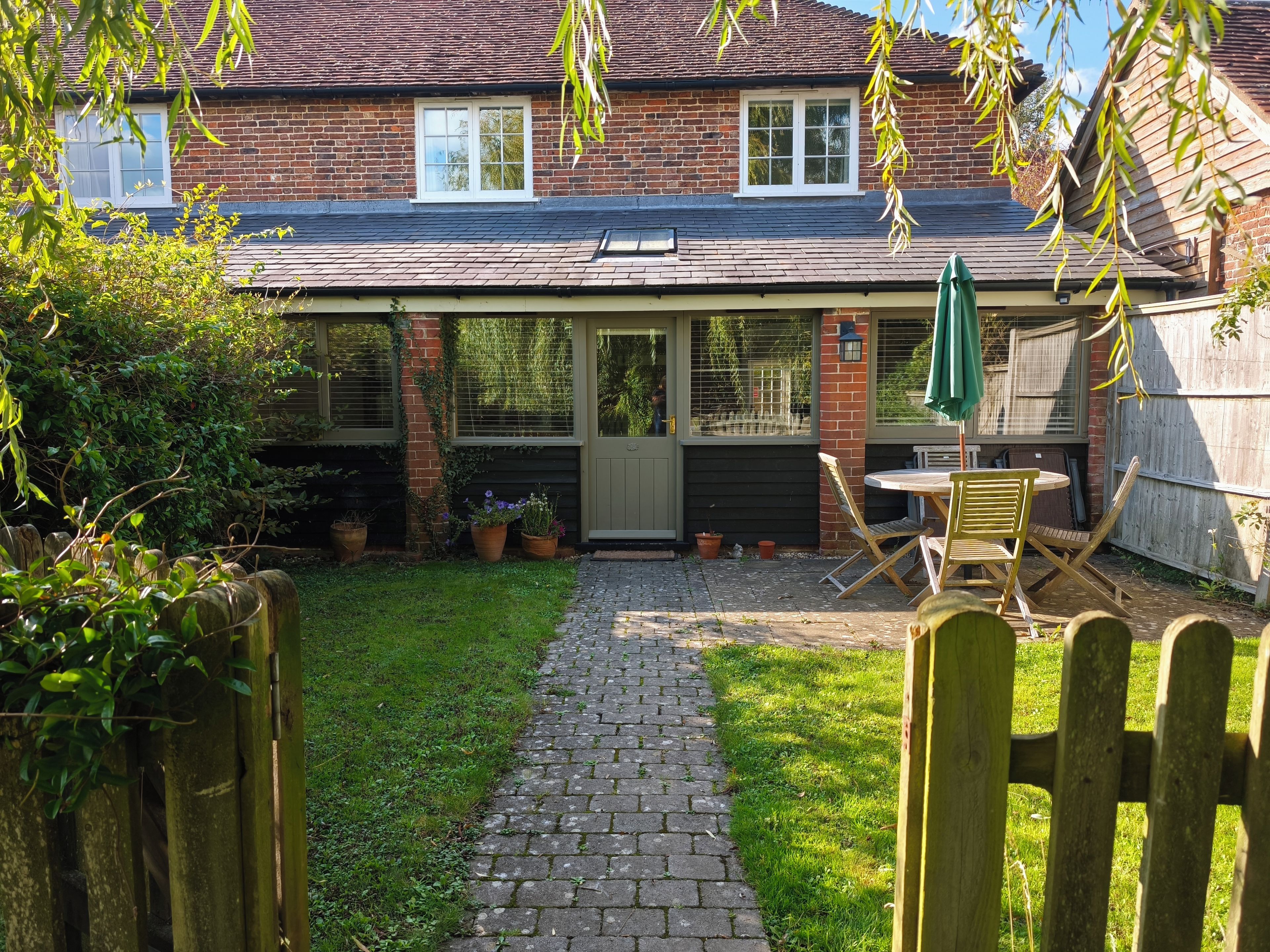 Une maison en briques avec un patio couvert, une clôture en bois et un chemin pavé menant à une porte.