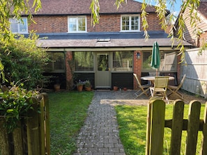 A brick house with a covered patio, a wooden fence, and a paved pathway leading to a door. - Barley cottage ,(granarycottages) in an old converted barn Chiddingly,lewes (Chiddingly , Lewes)
