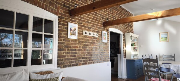 A room with a brick wall, wooden beams, a white door, a dining table with chairs, and a blue cabinet. - Barley cottage ,(granarycottages) in an old converted barn Chiddingly,lewes (Chiddingly , Lewes)