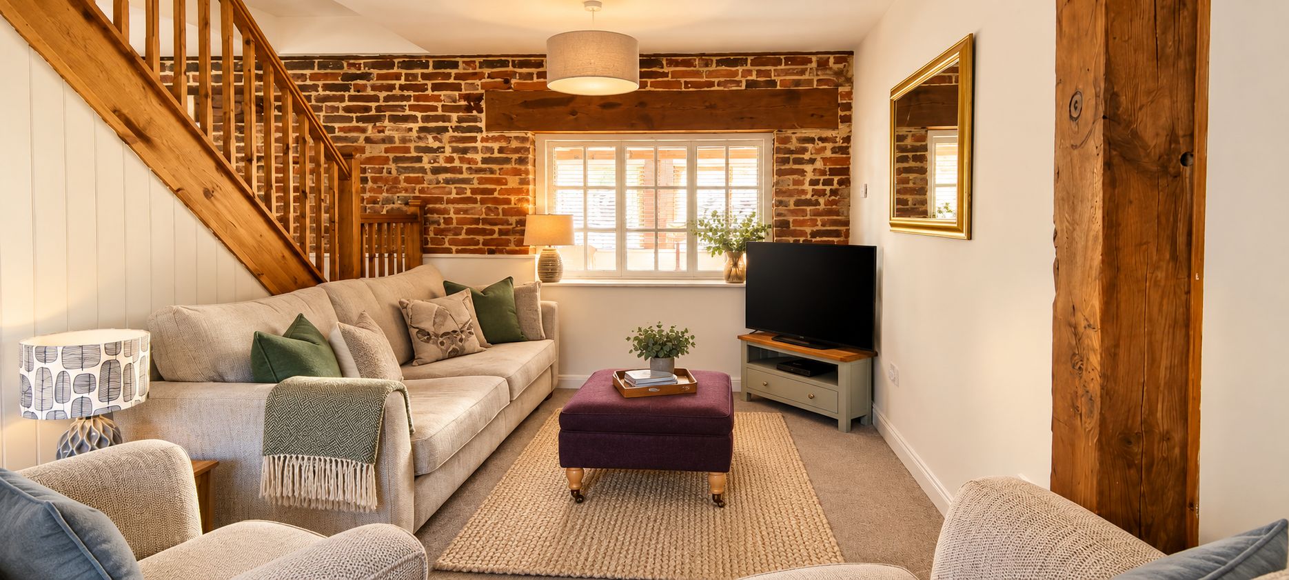 A living room with a brick wall, a wooden staircase, a sofa, a television, and a window with blinds.