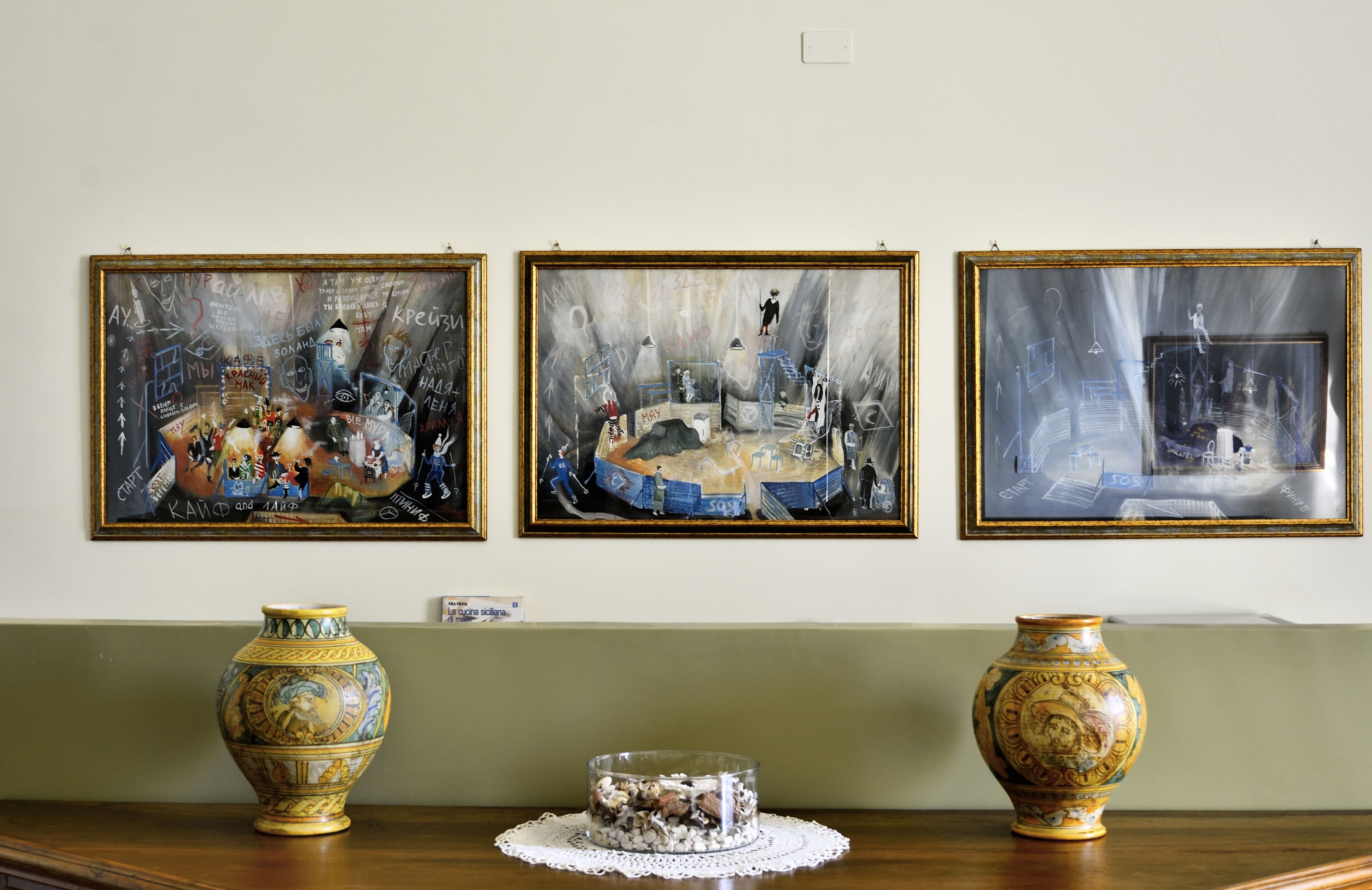 Tres obras de arte enmarcadas en una pared, una mesa de madera con dos jarrones decorativos, y un pequeño cuenco ornamental sobre la mesa.