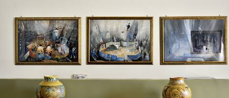 Tres obras de arte enmarcadas en una pared, una mesa de madera con dos jarrones decorativos, y un pequeño cuenco ornamental sobre la mesa.