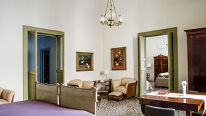 A hotel room with a bed, two armchairs, a dining table, and a chandelier. - Don Giovanni charming apartment (Catania)