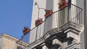 A building with a balcony featuring wrought iron railings and flower boxes. - Don Giovanni charming apartment (Catania)
