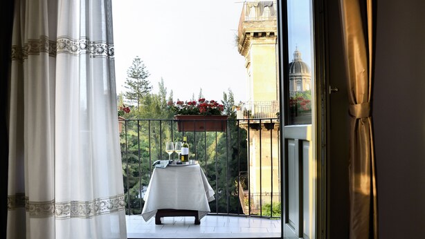 A balcony with a table set for two, a potted plant, and a view of a building with a dome. - Don Giovanni charming apartment (Catania)