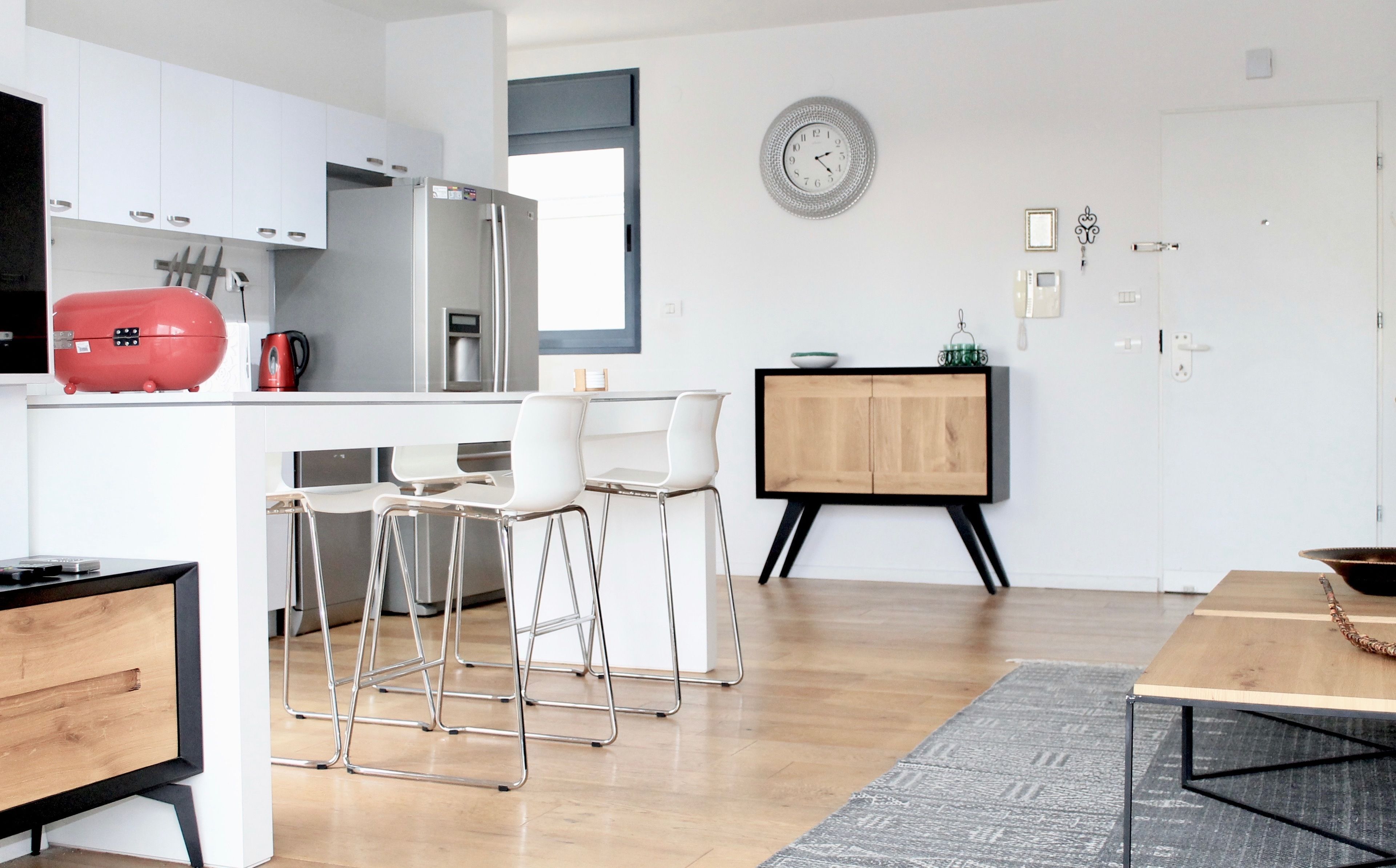 A modern kitchen with white cabinets, a red appliance, and a wooden dining table with bar stools.