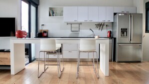 Eine moderne Küche mit weißen Schränken, einem Edelstahlkühlschrank und zwei weißen Barhocker.