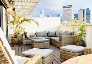 Una terraza en la azotea con mobiliario de mimbre, una planta en maceta y vistas al horizonte de la ciudad.