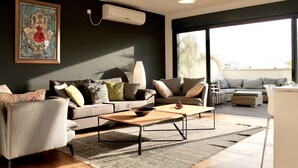 Ein modernes Wohnzimmer mit einer Sofagarnitur, einem Couchtisch und einem großen Fenster mit Blick ins Freie.