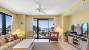 A living room with a sofa, armchairs, a coffee table, a TV, and a balcony with a view of the ocean. - 201C Beautiful Beachfront Condo (Orange Beach)