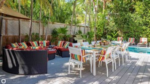 Un patio al aire libre con mobiliario de mimbre, una mesa de comedor preparada para cuatro personas y una piscina al fondo.