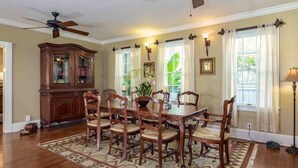 Une salle à manger avec une table et des chaises en bois, un ventilateur de plafond, une grande armoire en bois et un tapis à motifs.