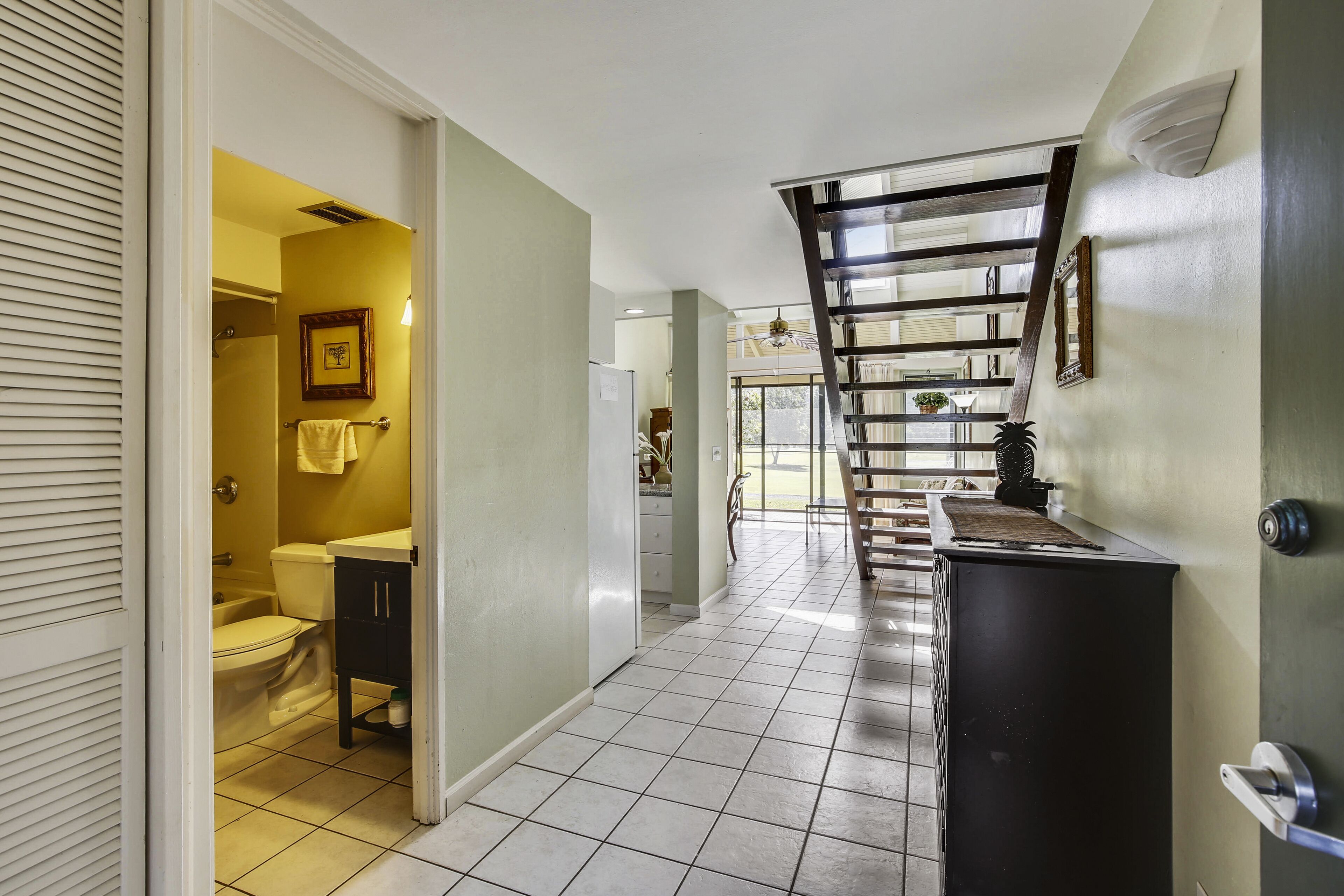 Un couloir avec un sol carrelé, un escalier et une porte donnant sur une salle de bain.
