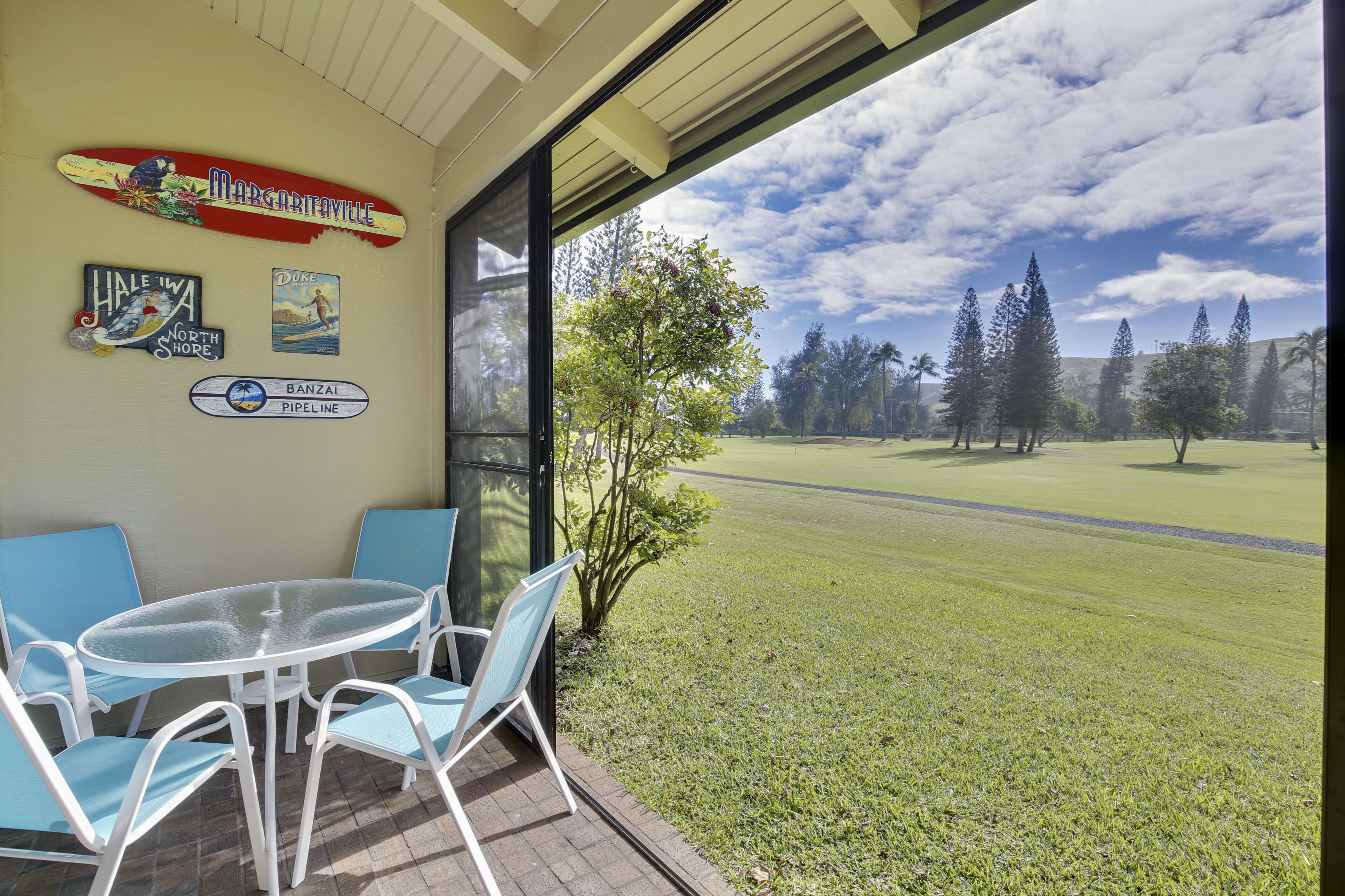 A room with a glass door leading to a golf course view, a table with chairs, and wall decorations including a sign for 'Margaritaville North Shore'.