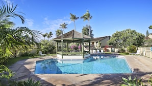 Une piscine avec un kiosque, des palmiers et une maison en arrière-plan.