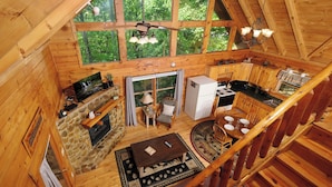 Une cabane en bois comprenant un coin repas, une cuisine et une cheminée en pierre.