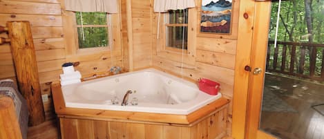 A wooden cabin with a large bathtub, two windows with curtains, and a door leading to an outdoor deck.