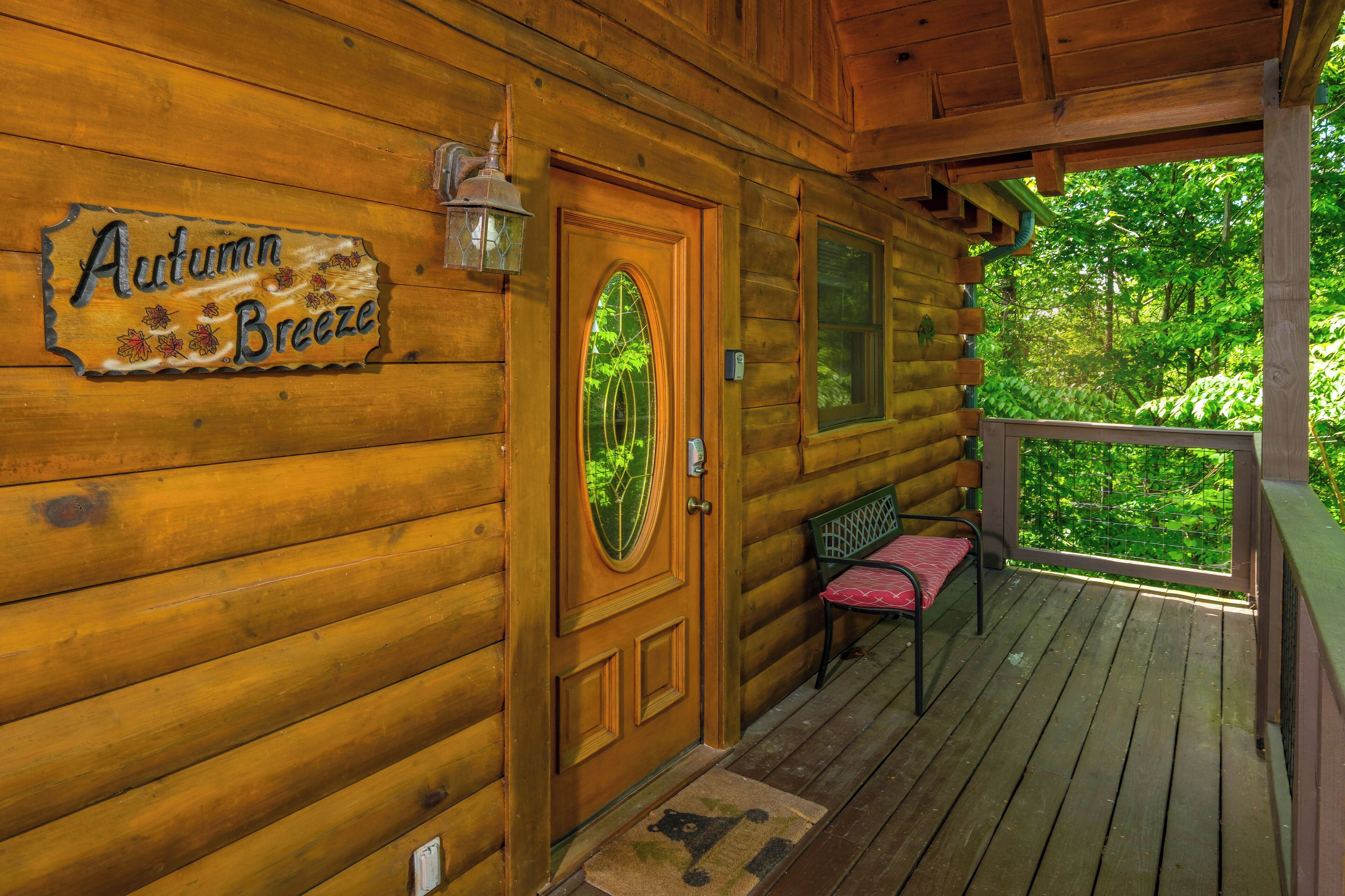 Una cabana de fusta amb un rètol a la porta que diu "Autumn Breeze", una banca al porxo i una vista de vegetació a l'exterior.