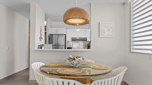 A modern dining area with a glass table, white chairs, and a woven pendant light.