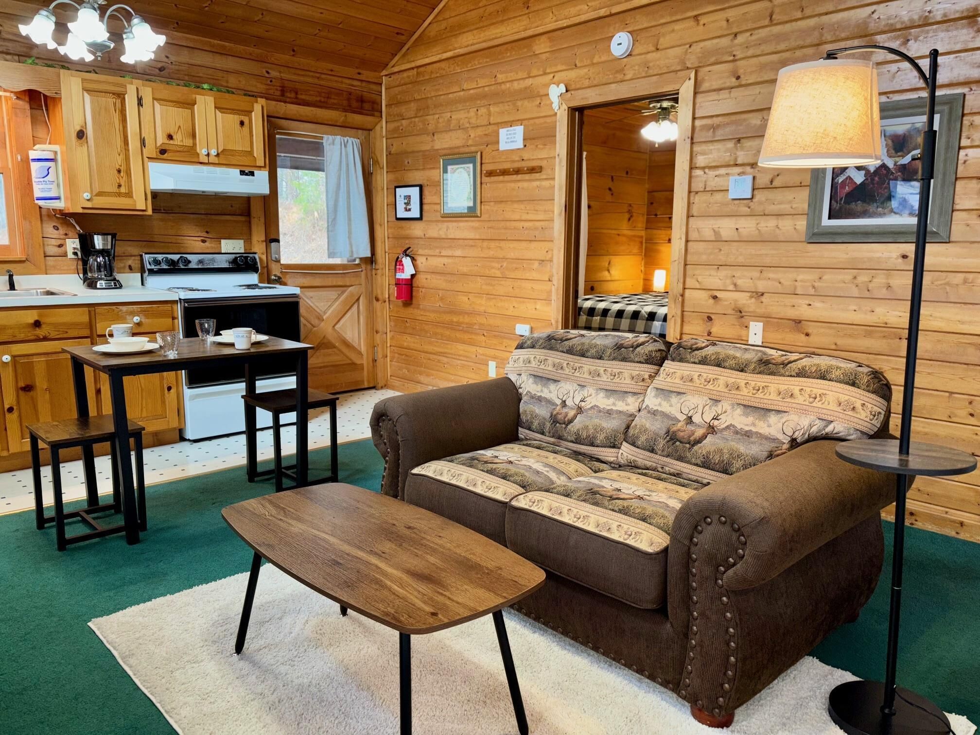 A cozy cabin interior with a wooden interior, a sofa with elk print cushions, a dining table, and a kitchenette.