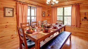 Une salle à manger aménagée dans une cabane en bois, avec une table en bois dressée pour quatre personnes, entourée de chaises.