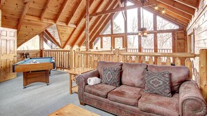 Un intérieur chaleureux de chalet en bois, avec une table de billard, un canapé en cuir et une terrasse en bois.