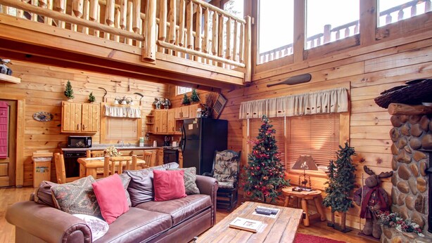 L’intérieur chaleureux d’un chalet avec un coin repas en bois, un canapé en cuir, un sapin de Noël et une cheminée en pierre.