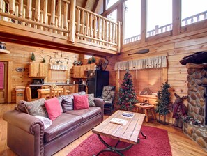 A cozy cabin interior with a wooden dining area, a leather sofa, a Christmas tree, and a stone fireplace. - Pool table, hot tub, and adorable 1BR log cabin for a perfect stay! (Sevierville)