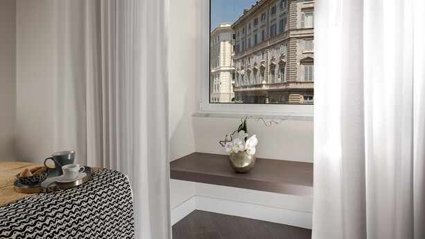 A hotel room with a view of a historic building, a small table with a cup and saucer, and a vase with flowers on a shelf. - Charme 308 (Rome)