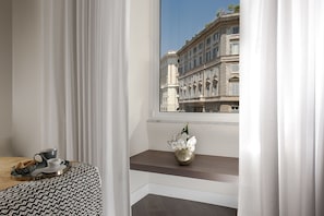 Ein Hotelzimmer mit Blick auf ein historisches Gebäude, ein kleiner Tisch mit Tasse und Untertasse sowie eine Vase mit Blumen auf einem Regal.