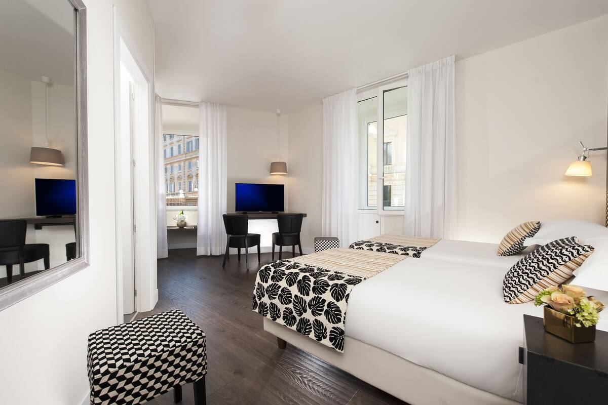 A hotel room with a large bed, a desk, a chair, a TV, and a window with curtains.