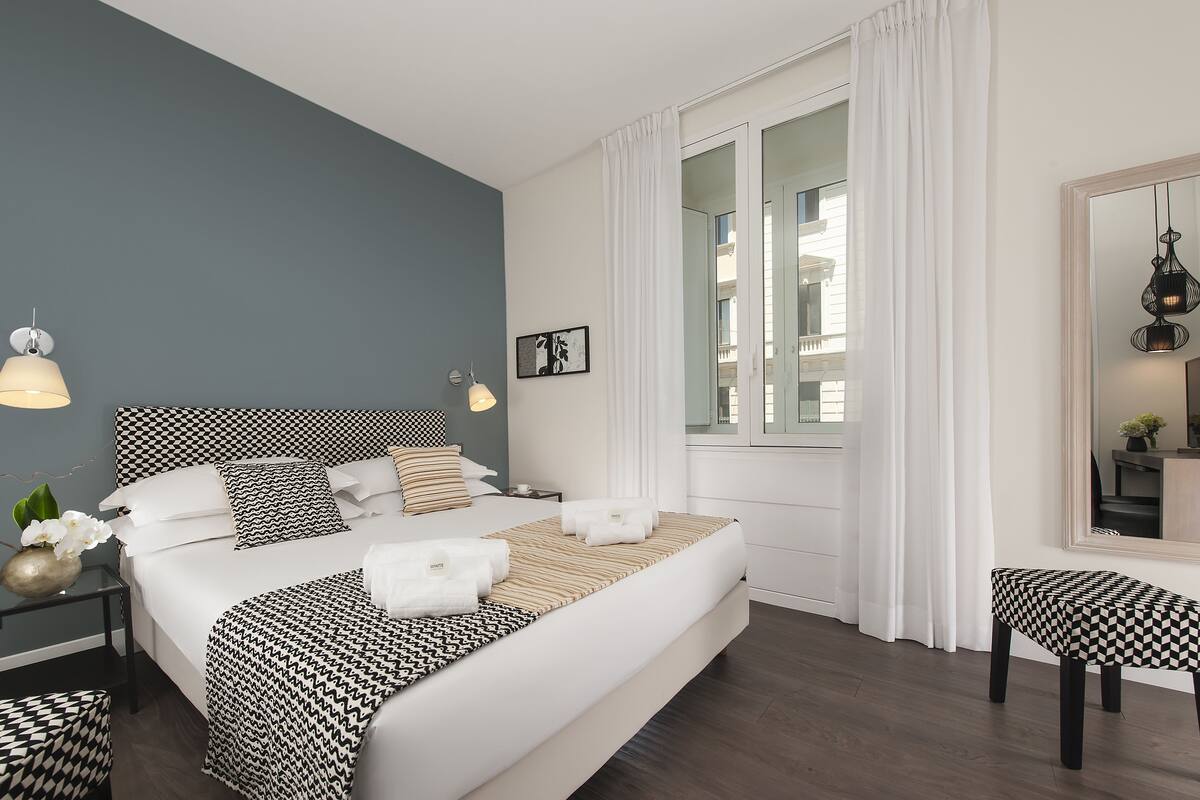 A modern bedroom with a large bed, bedside tables, a chair, and a mirror.