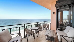 A balcony with wicker furniture, a wooden table, and a view of the ocean.