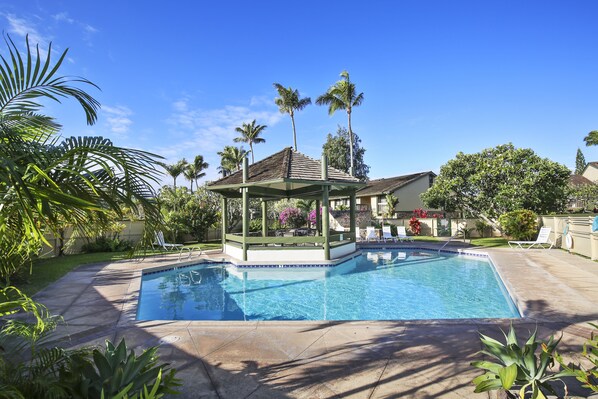 A swimming pool with a gazebo, palm trees, and a house in the background.