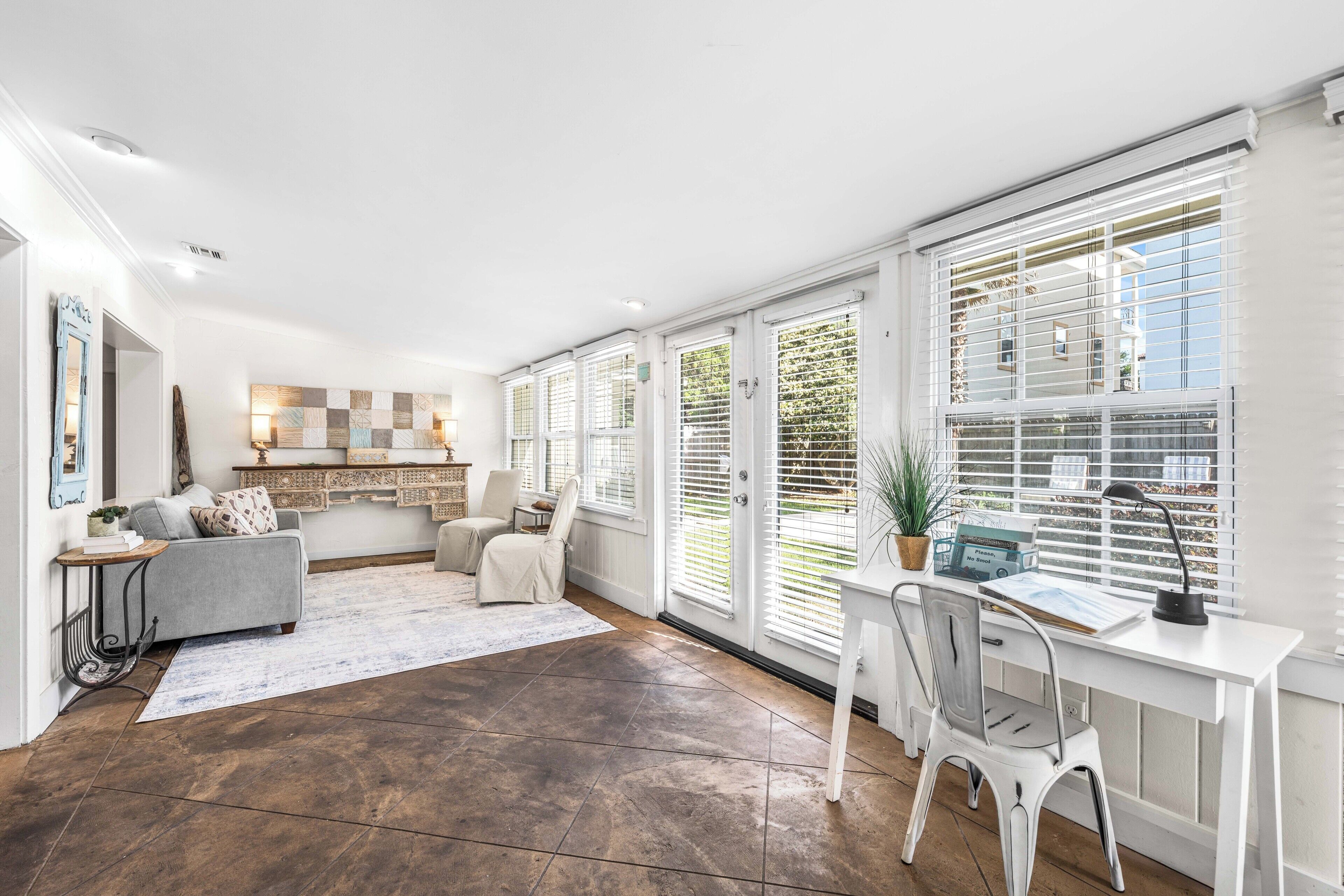 A spacious room with a large window, a desk, a chair, a sofa, and a small table.