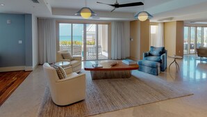 A spacious living room with a large window, a ceiling fan, and a view of the ocean. - Astonishing Oceanfront Residence Located at The Ritz-Carlton, Grand Cayman (Seven Mile Beach)