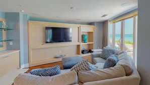 A modern living room with a large flat-screen TV, comfortable seating, and a view of the ocean. - Astonishing Oceanfront Residence Located at The Ritz-Carlton, Grand Cayman (Seven Mile Beach)