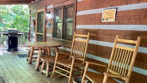 A wooden deck with a table and chairs, a barbecue grill, and a welcome sign on the wall. - 1BR log cabin (sleeps 4) with screened-in hot tub and 1 free Dollywood ticket! (Sevierville)