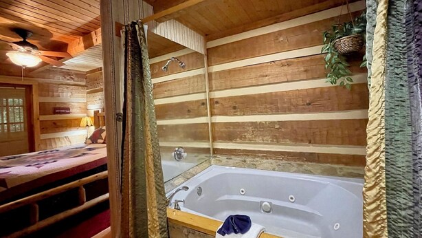 A log cabin interior with a wooden interior, a stone-walled bathroom with a bathtub, and a bed with a wooden headboard. - 1BR log cabin (sleeps 4) with screened-in hot tub and 1 free Dollywood ticket! (Sevierville)