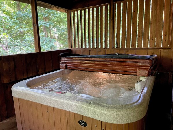 A hot tub with a wooden exterior, a wooden bench, and a view of trees through a window. - 1BR log cabin (sleeps 4) with screened-in hot tub and 1 free Dollywood ticket! (Sevierville)
