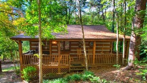 A rustic cabin with a wooden deck, surrounded by trees. - 1BR log cabin (sleeps 4) with screened-in hot tub and 1 free Dollywood ticket! (Sevierville)