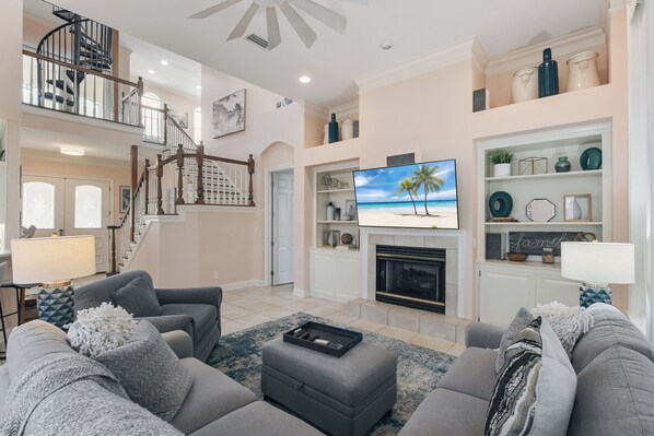A spacious living room with a fireplace, a television, and a staircase leading to an upper level.