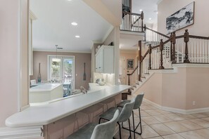 A kitchen with a large island, bar stools, and a staircase leading to an upper level.