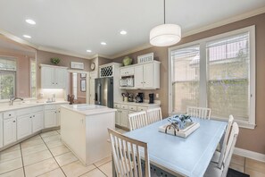 A modern kitchen with white cabinetry, a central island, and a dining area with a blue table and white chairs.