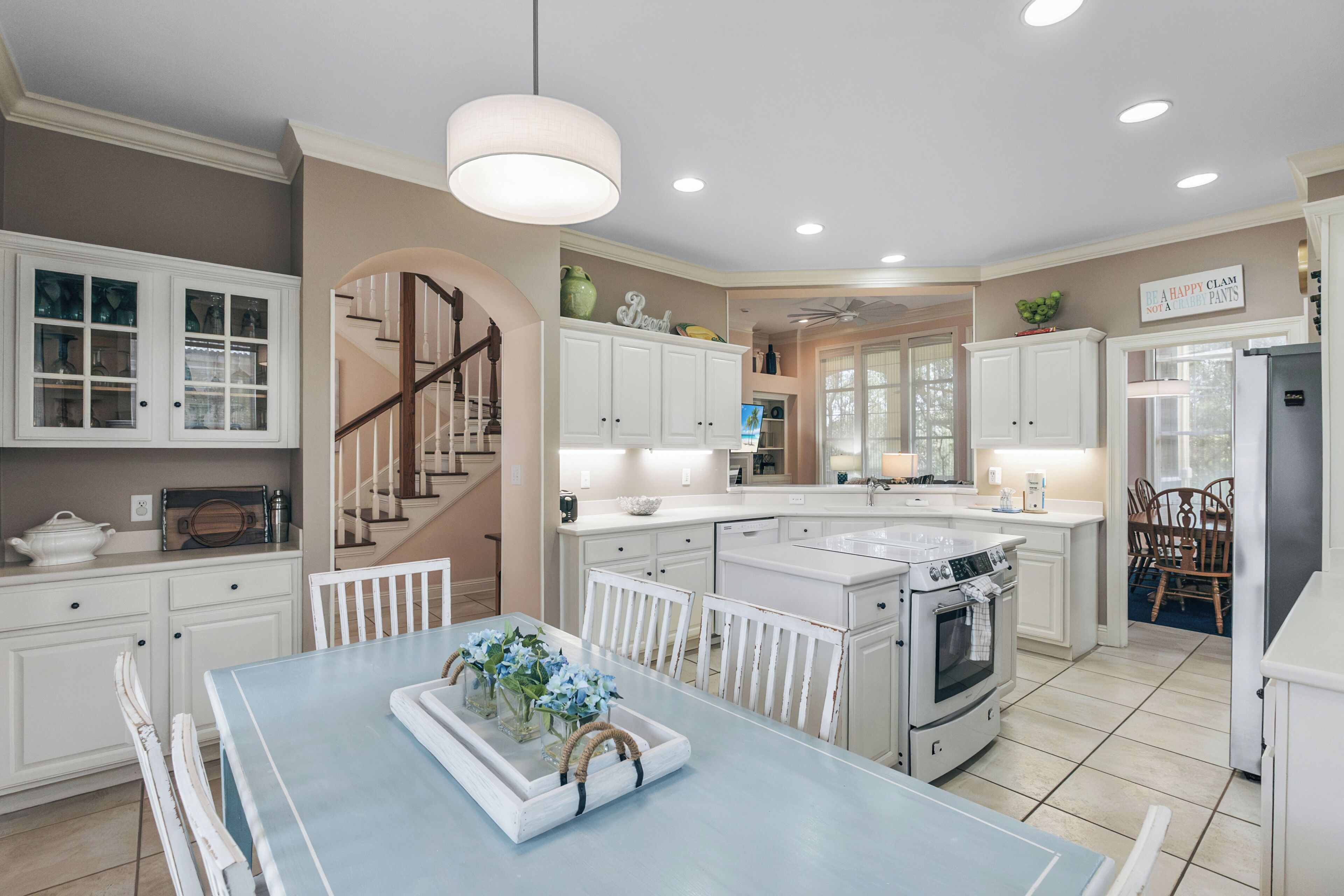 A spacious kitchen with white cabinetry, a central island, and a dining area with a blue table.