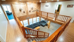 A spacious loft-style living area with a wooden staircase, a sectional sofa, and a view of the outdoors. - Laurel View Retreat - Spacious Private Estate Experience (Hopwood)