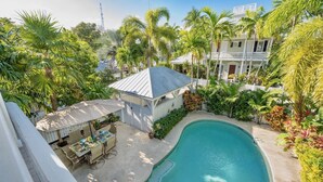 A pool area with a small gazebo, dining table, and chairs, surrounded by lush tropical vegetation and a large building in the background. - **BRISA FRESCA @ THE ANNEX** Airy Home + Last Key White Glove Service... (Key West)